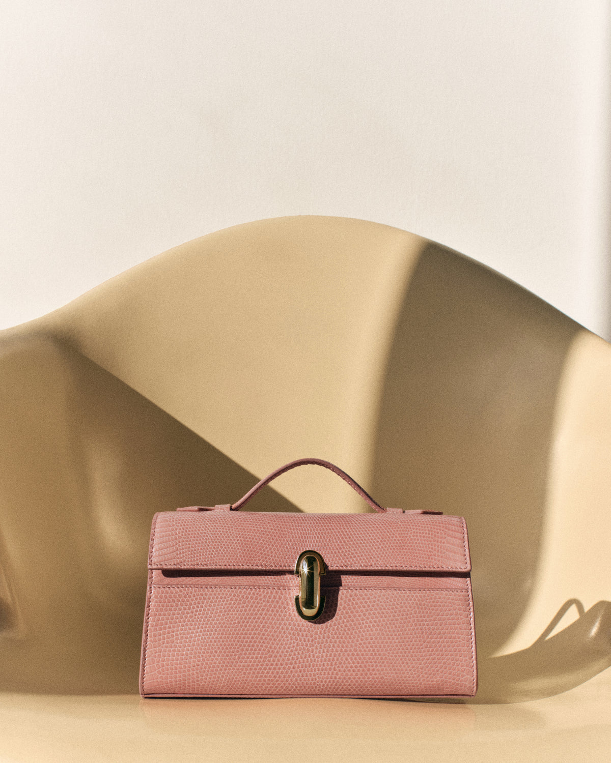 campaign front view of a blush pink lizard bag with a gold clasp on an off white background