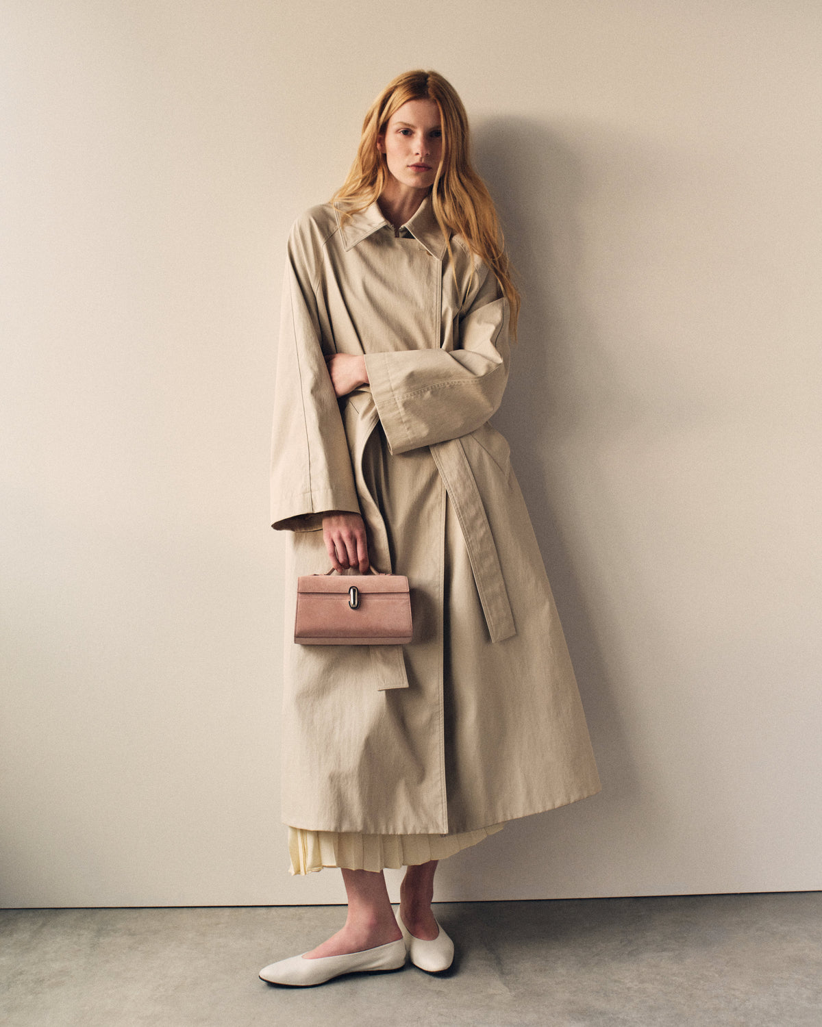campaign on model image of a blush pink suede bag with a silver clasp on a beige background