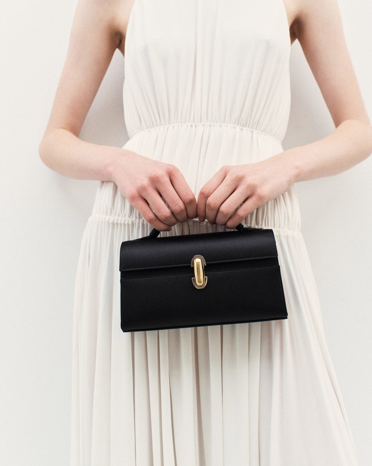 on model view of black satin bag with silver and gold clasp on a white background