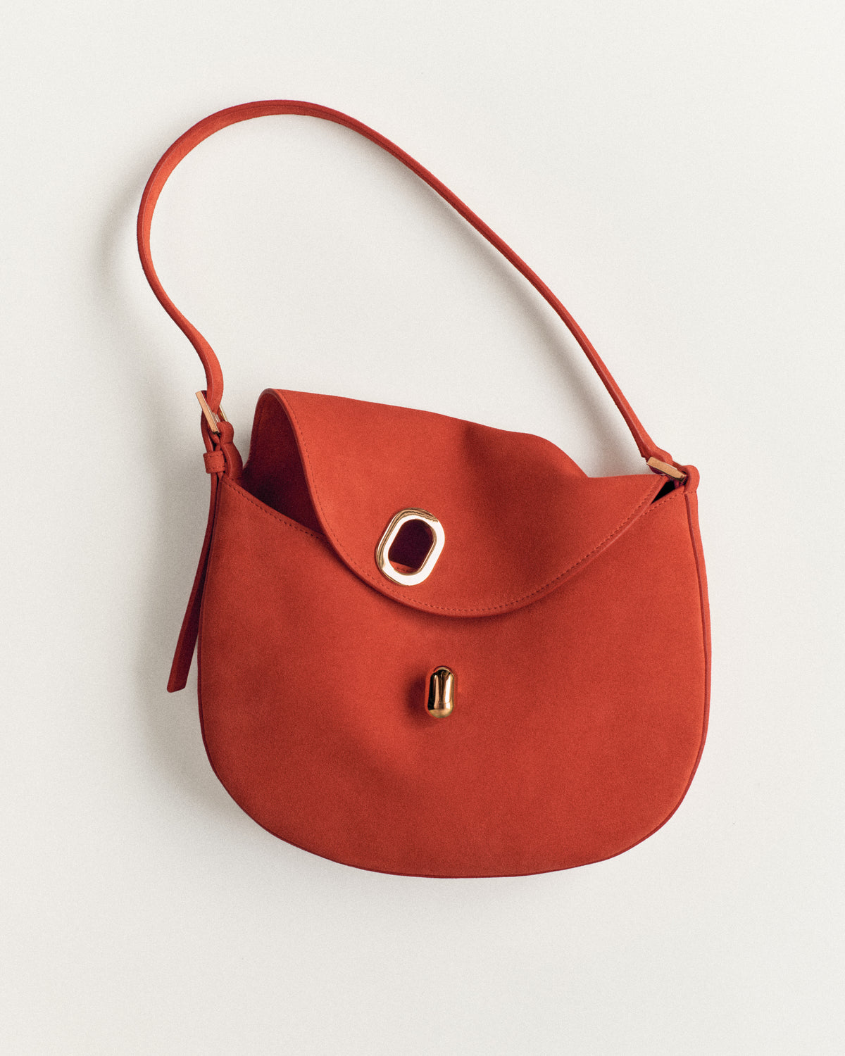 campaign image of a poppy red suede bag with a gold clasp on a white background