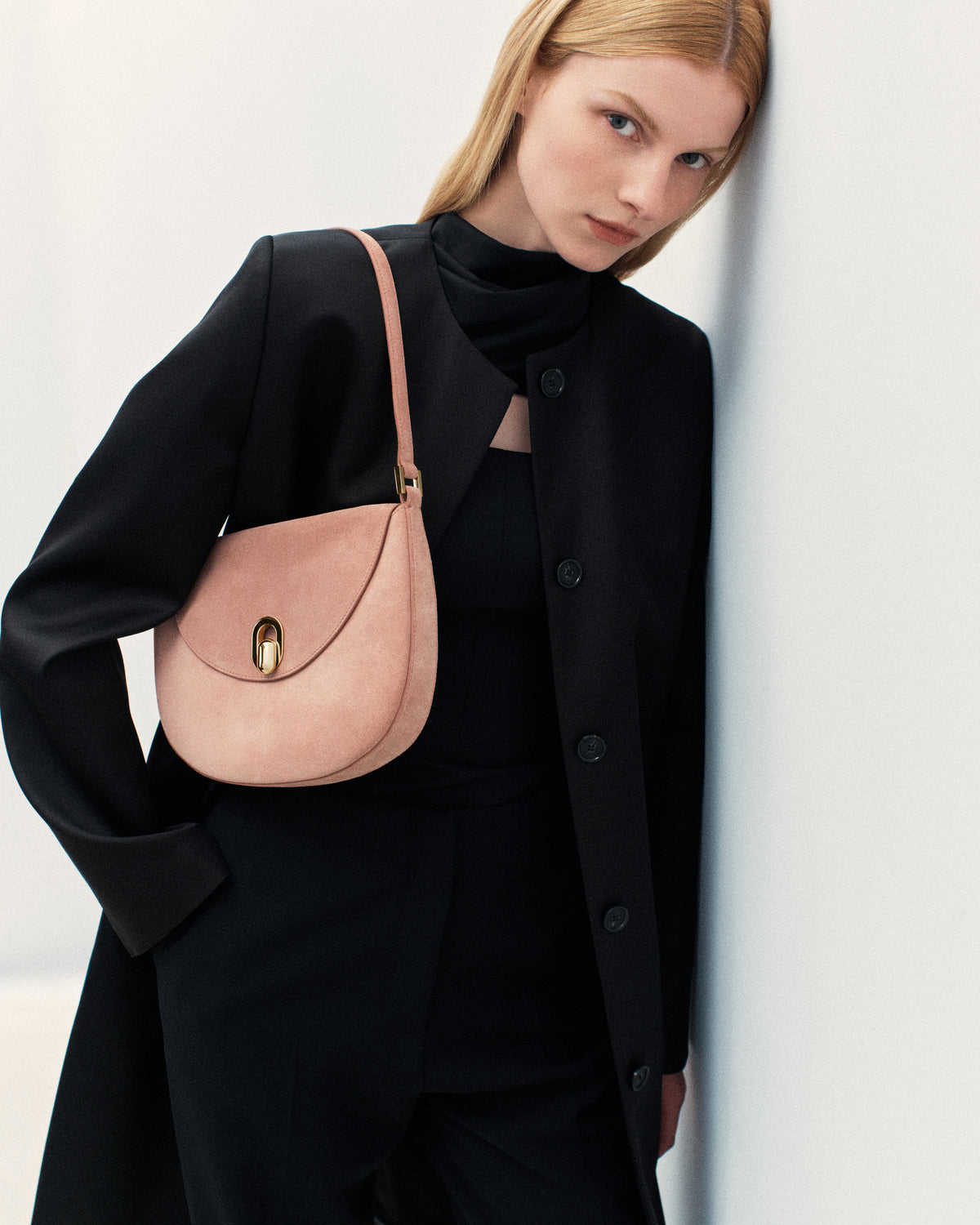 campaign on model image of a blush pink suede bag with gold clasp on a white background