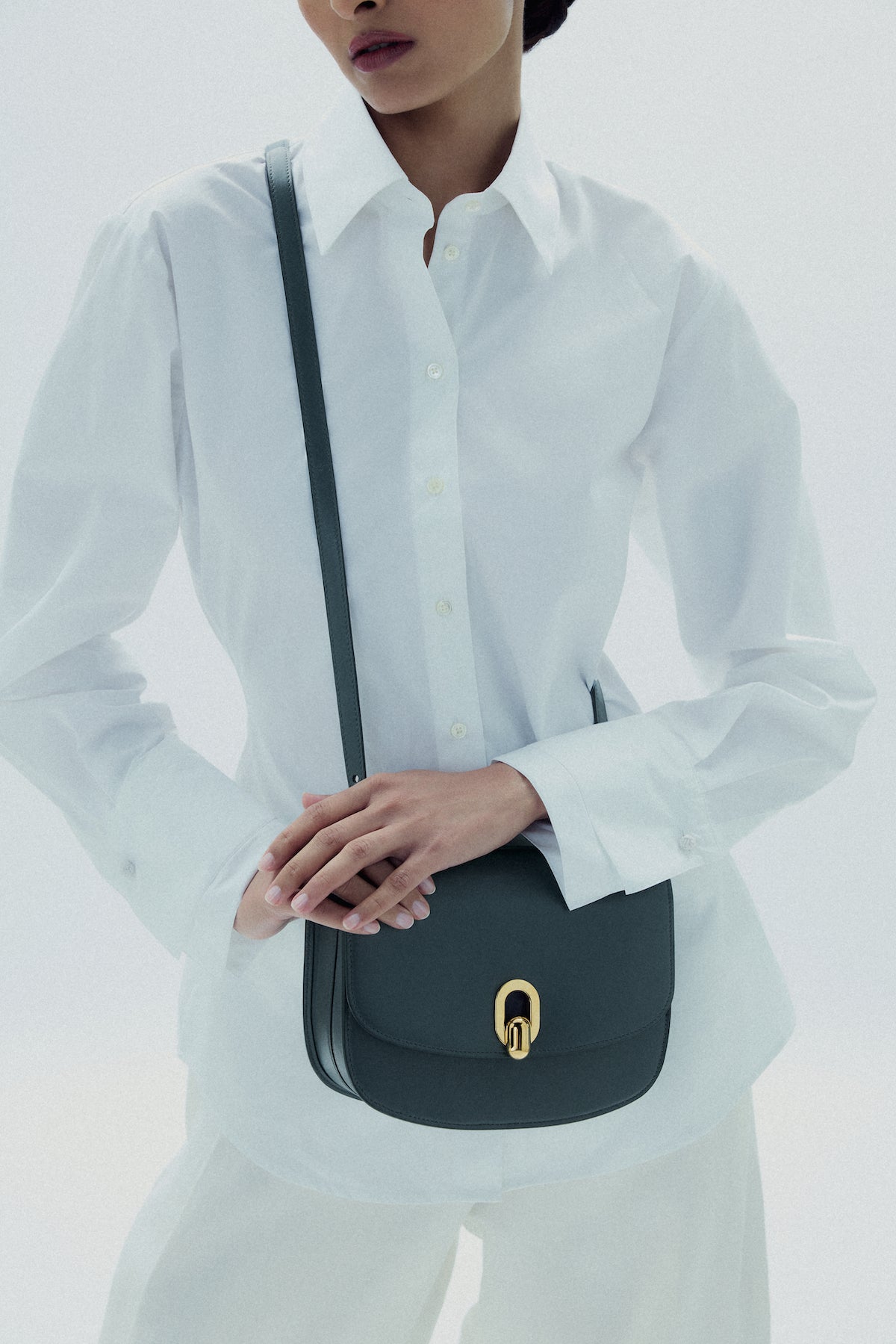 on model image of a storm blue leather bag with gold hardware on a white background