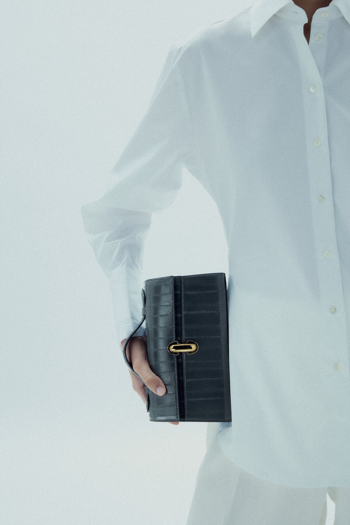 on model image of a storm blue eel bag with a gold clasp on a white background