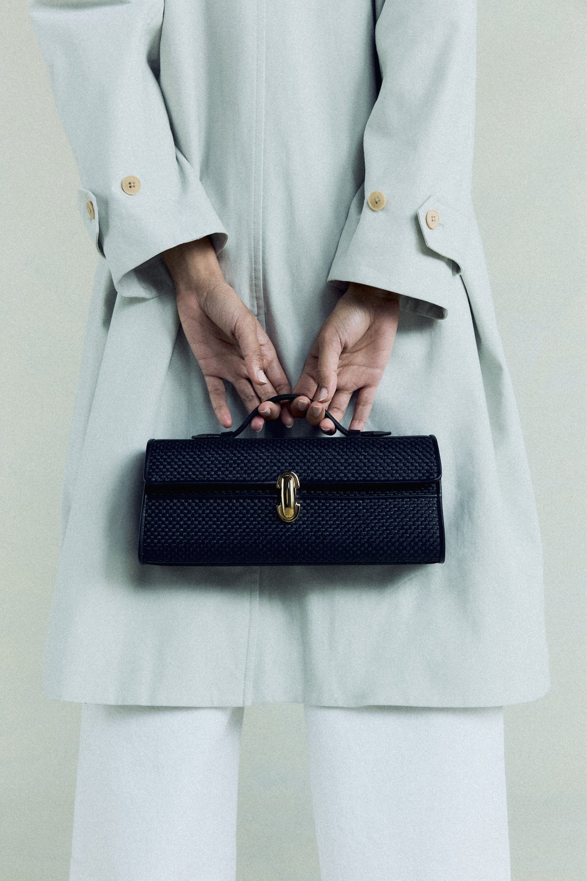 campaign on model image of a black raffia bag with leather trim with a gold clasp on an off white background
