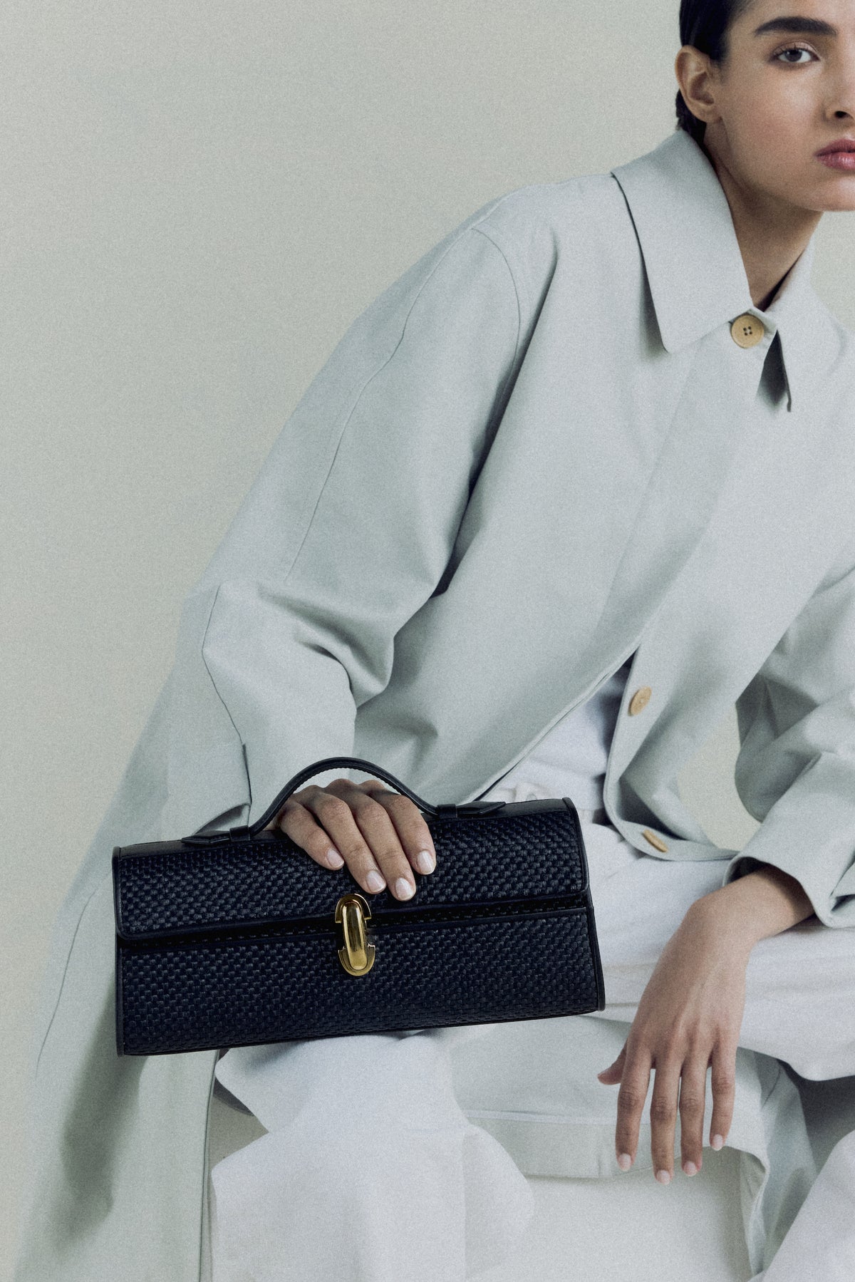 campaign on model image of a black raffia bag with leather trim with a gold clasp on an off white background