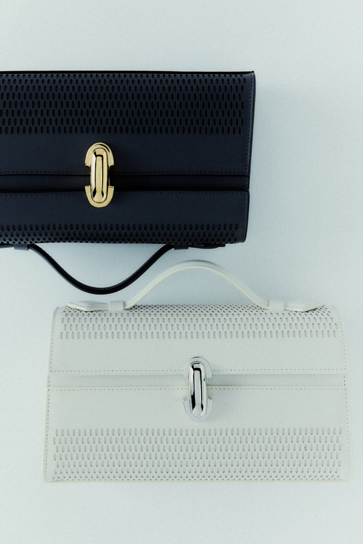 campaign image of a black leather lasercut bag with a gold clasp and an ivory leather lasercut with a silver clasp on an off white background