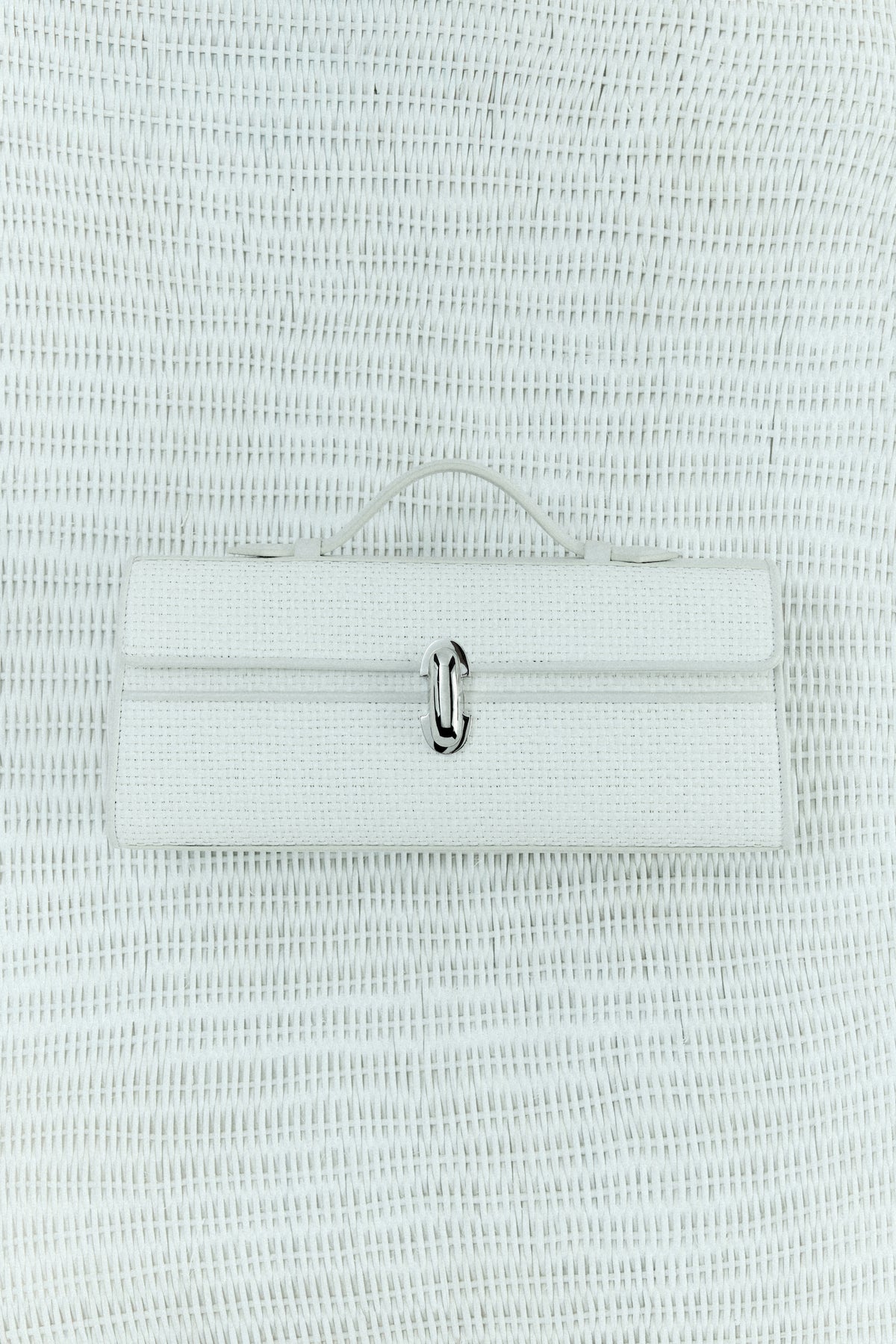 campaign image of an ivory raffia bag with leather trim with a silver clasp on an ivory raffia background