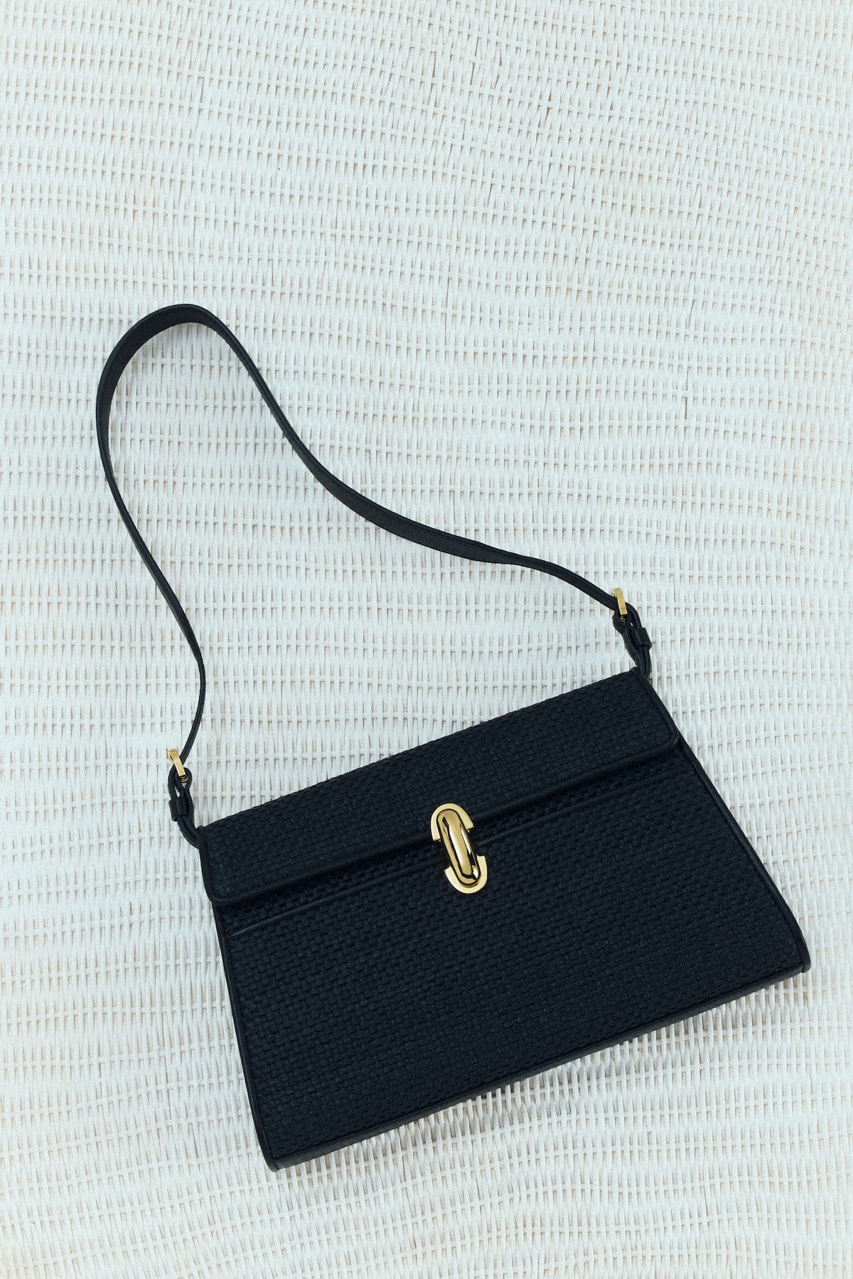 campaign image of a black raffia bag with leather trim with gold clasp on a white raffia background