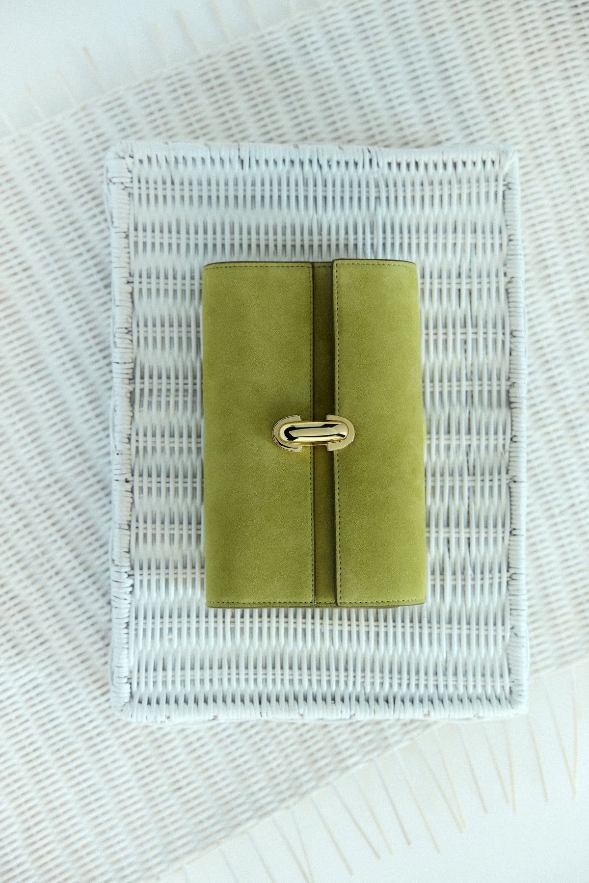 campaign image of a chartreuse green suede with a gold clasp on an ivory raffia background