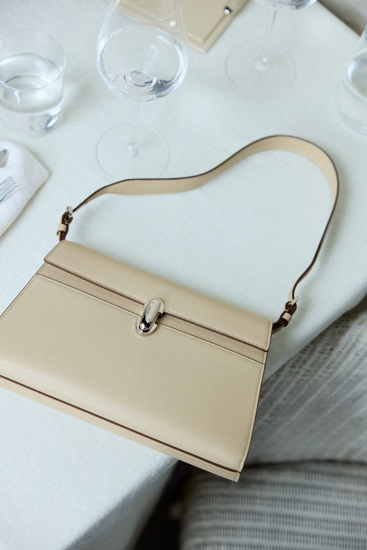 campaign image of a bone beige bag with a silver clasp on a dining table