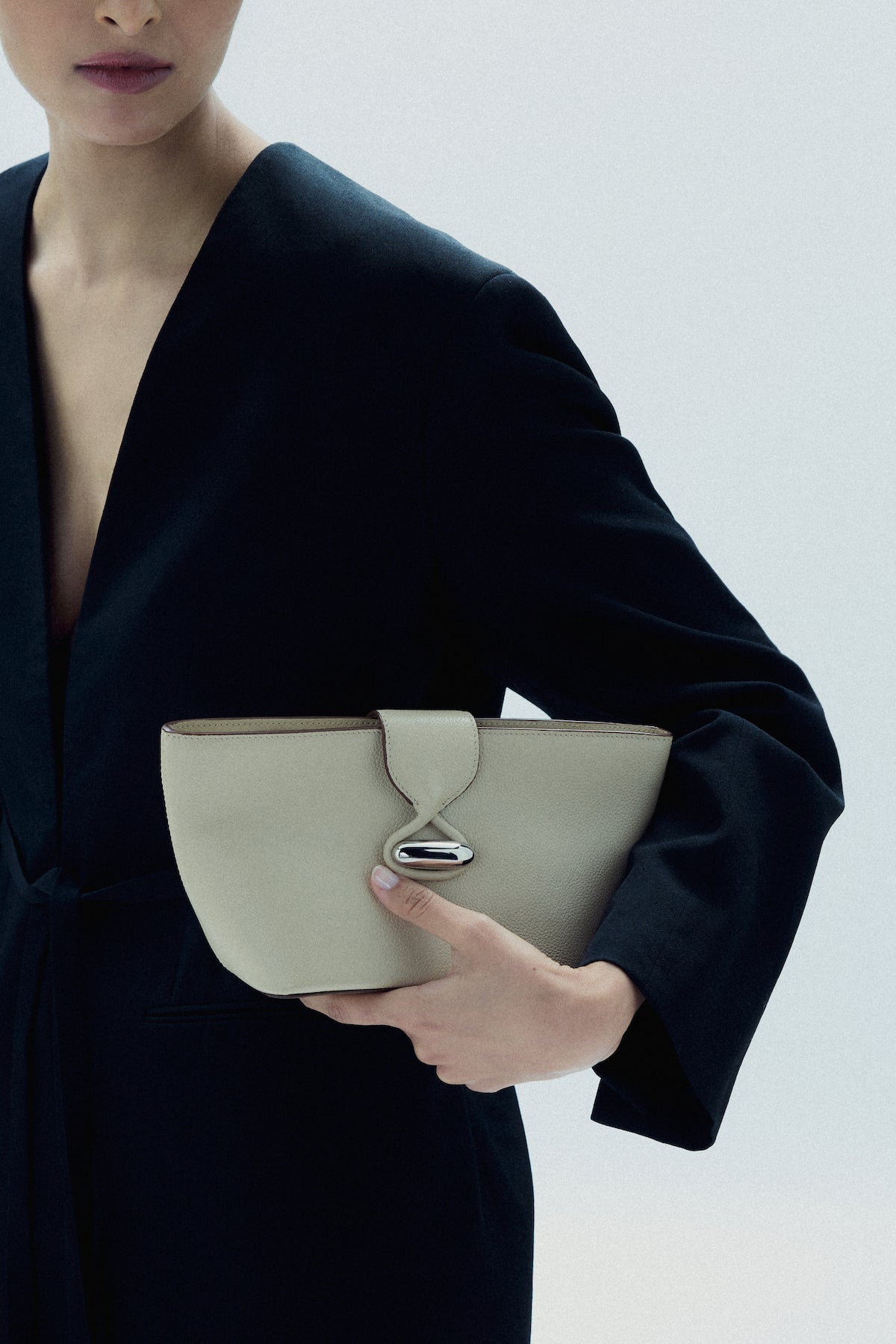 on model image of a bone beige leather pouch with silver hardware on a white background