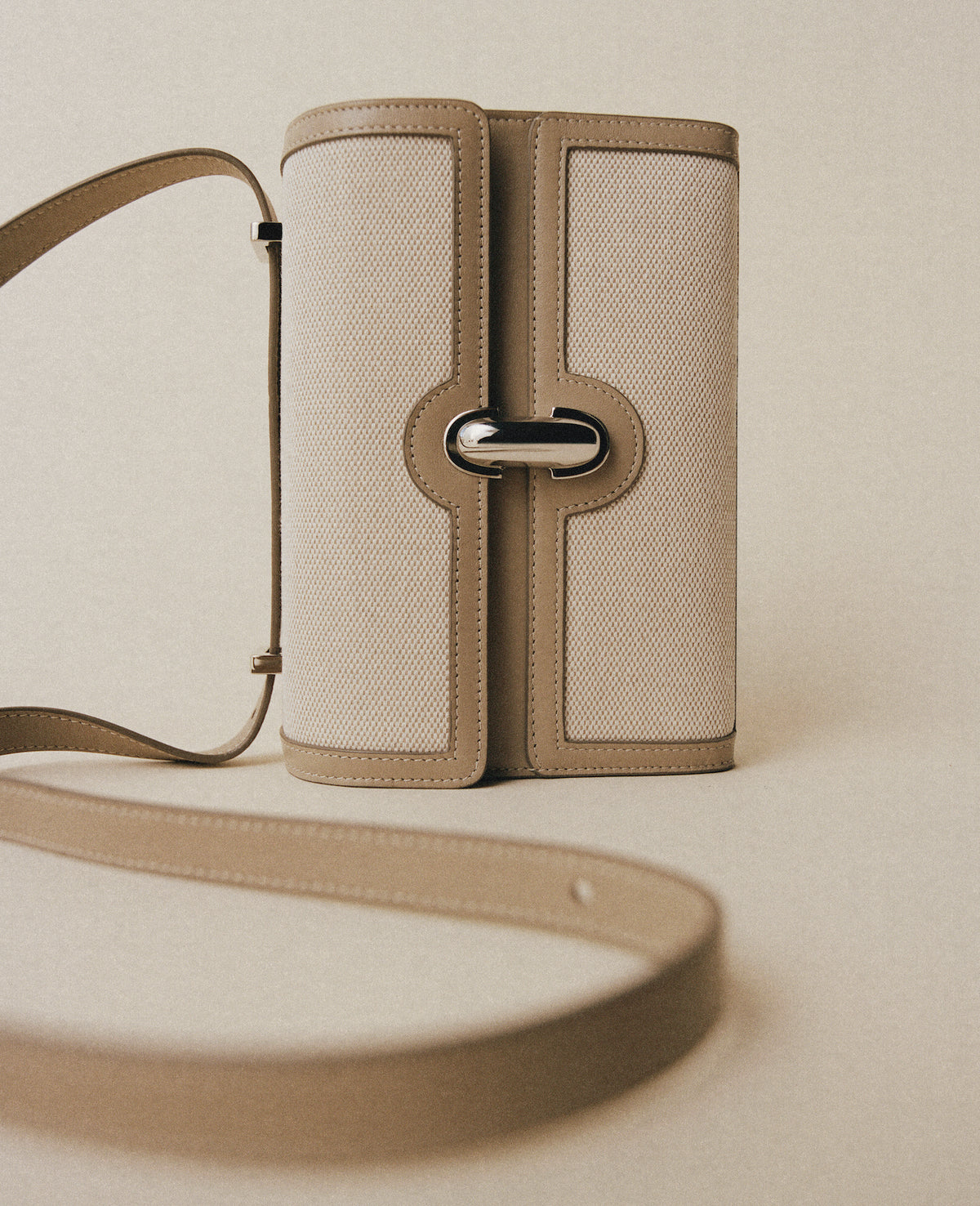 campaign view of a beige canvas with leather trim with a silver clasp on an off white background