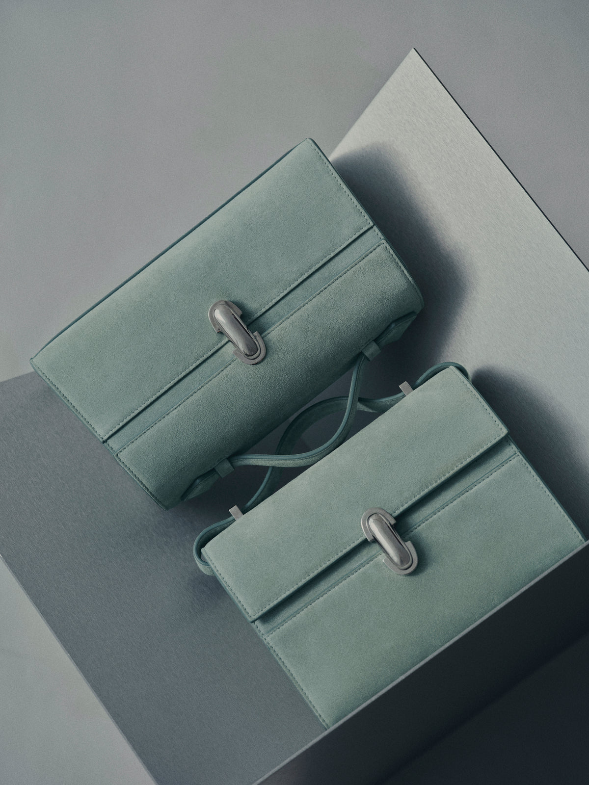 campaign image of two mist green suede bags with silver clasps on a grey background