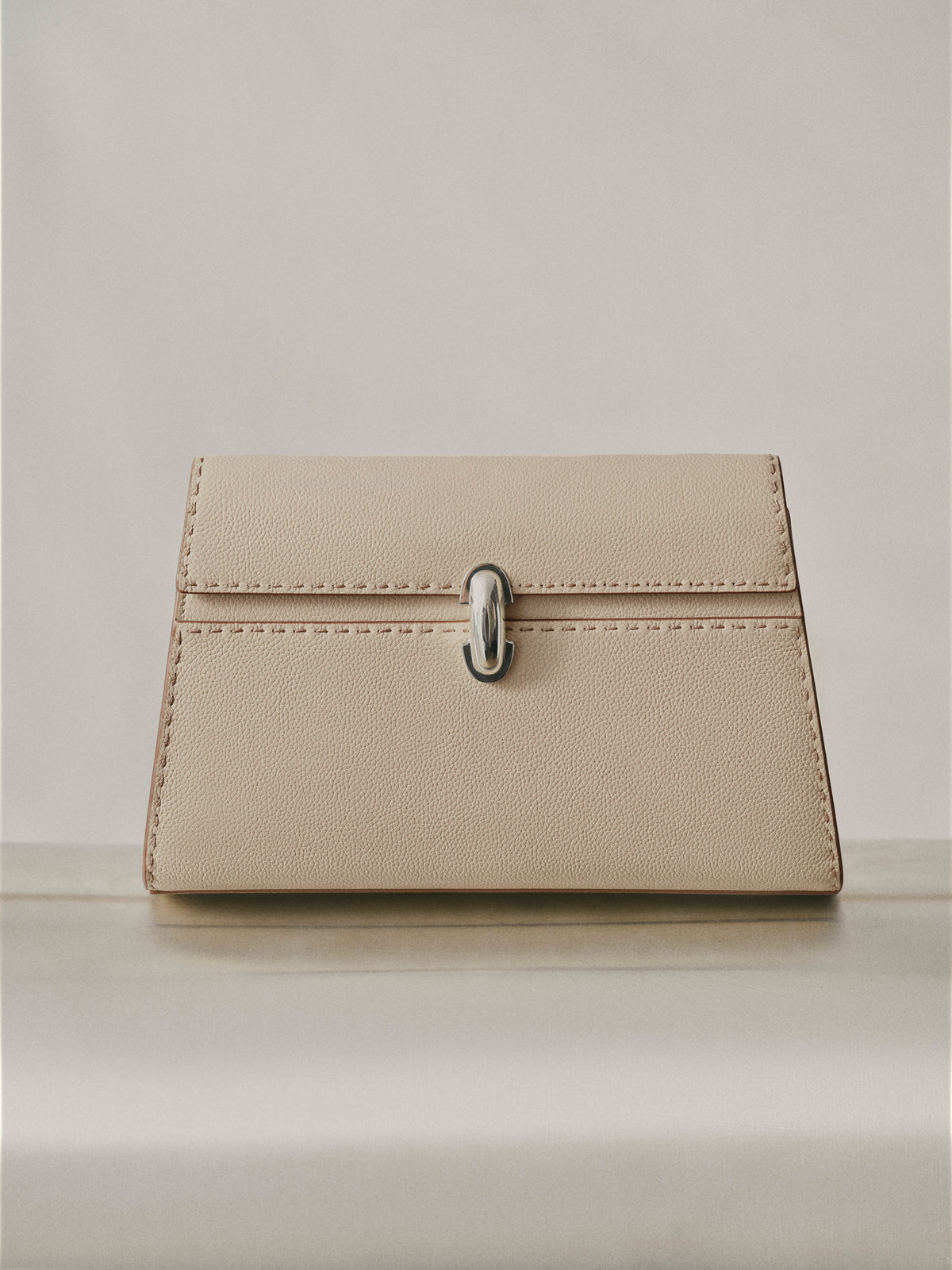 campaign image of bone beige bag with silver clasp and hand stitching on an off white background