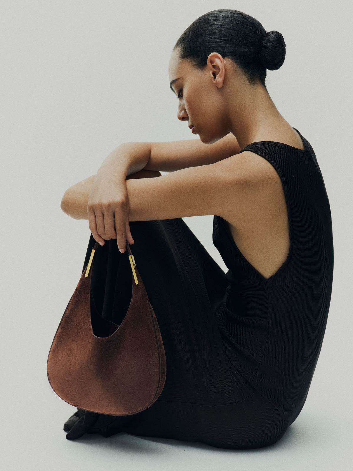 campaign on model image of espresso brown suede bag with gold hardware on a white background