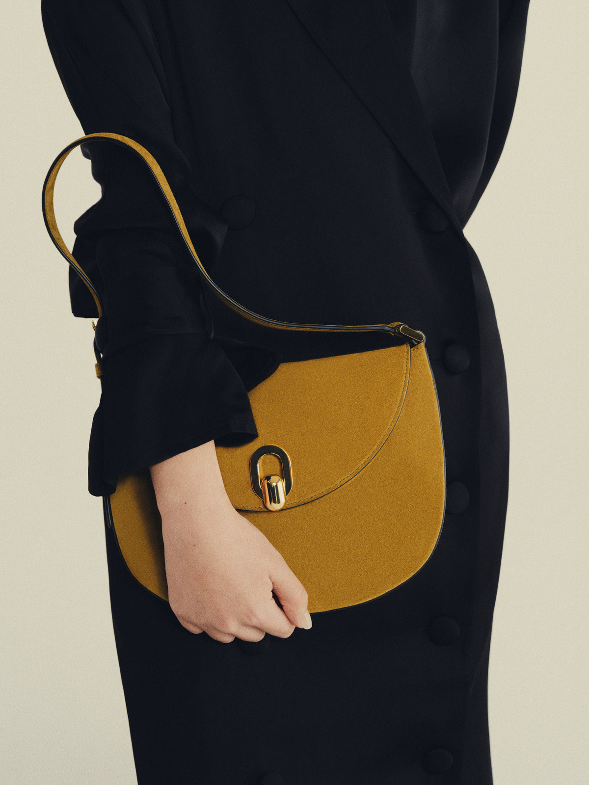 on model image of sepia brown suede bag with gold clasp on an off white background