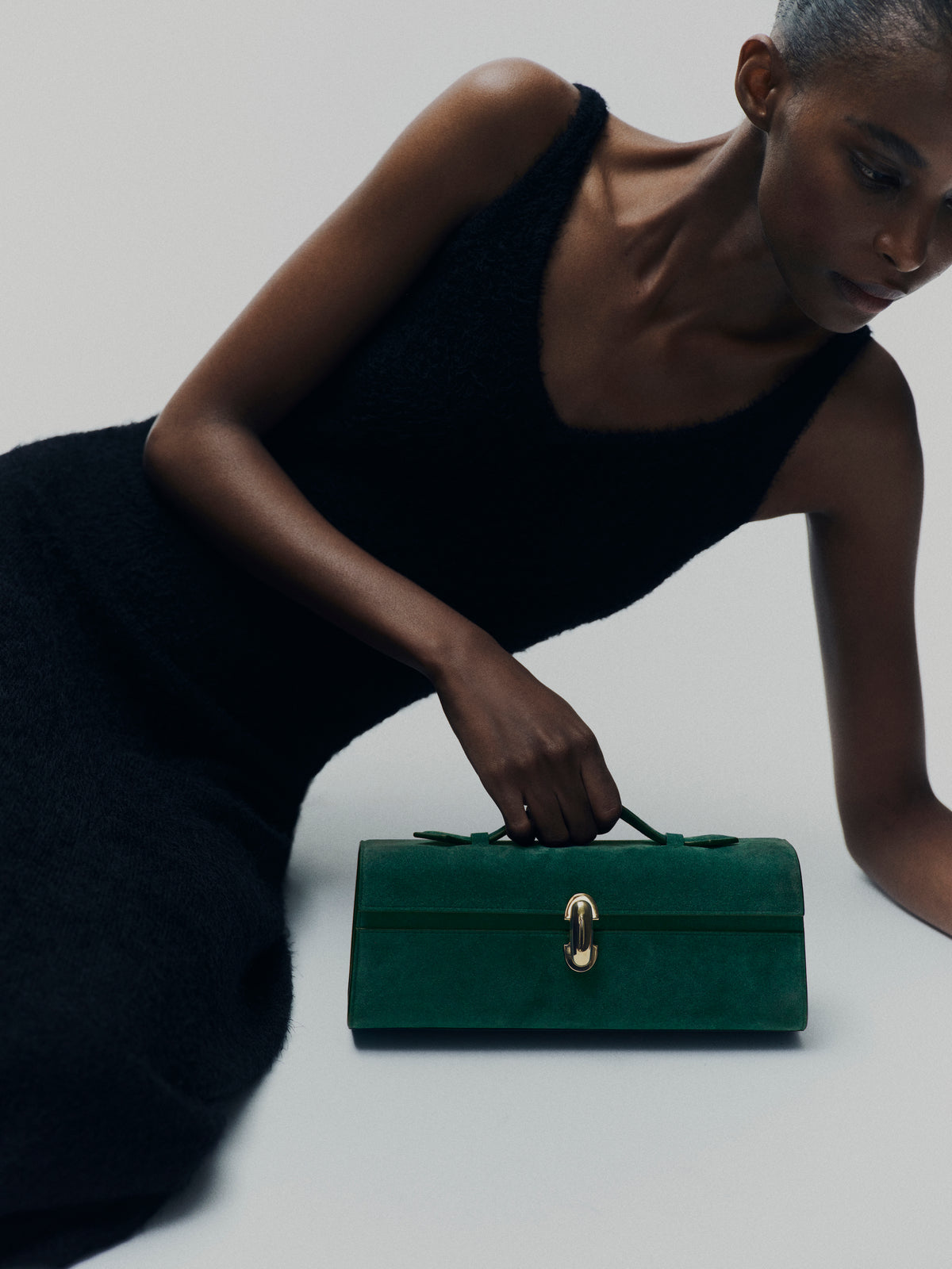 campaign on model image of pine green suede bag with gold clasp on a white background