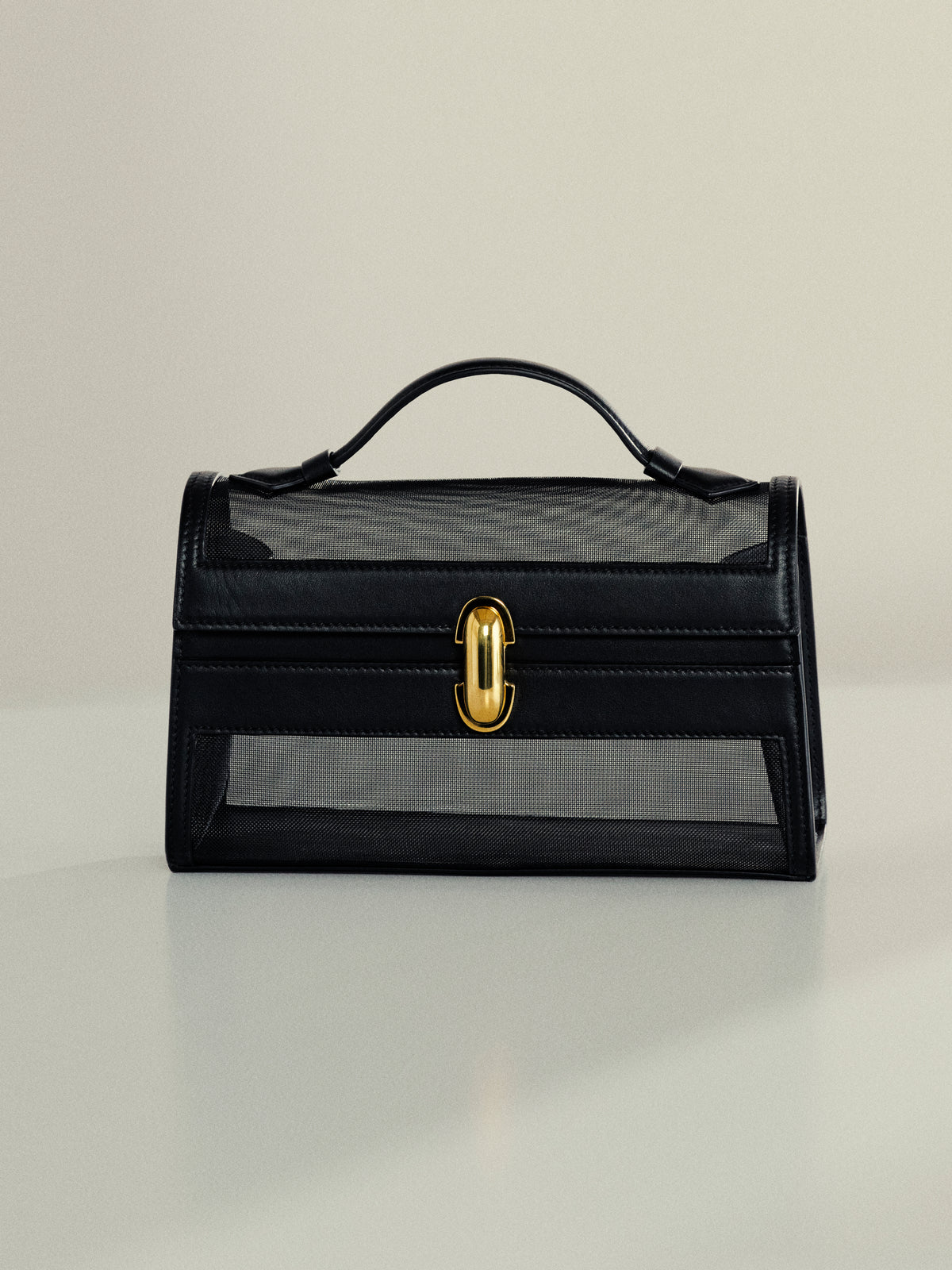 front view of black mesh bag with leather trim and gold clasp on an off white background