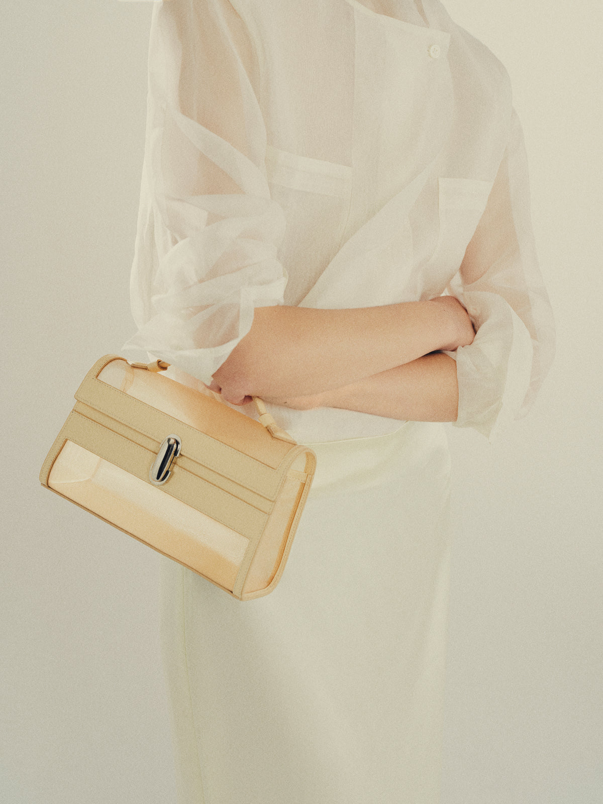 on model image of ecru mesh bag with leather trim and silver clasp on an off white background