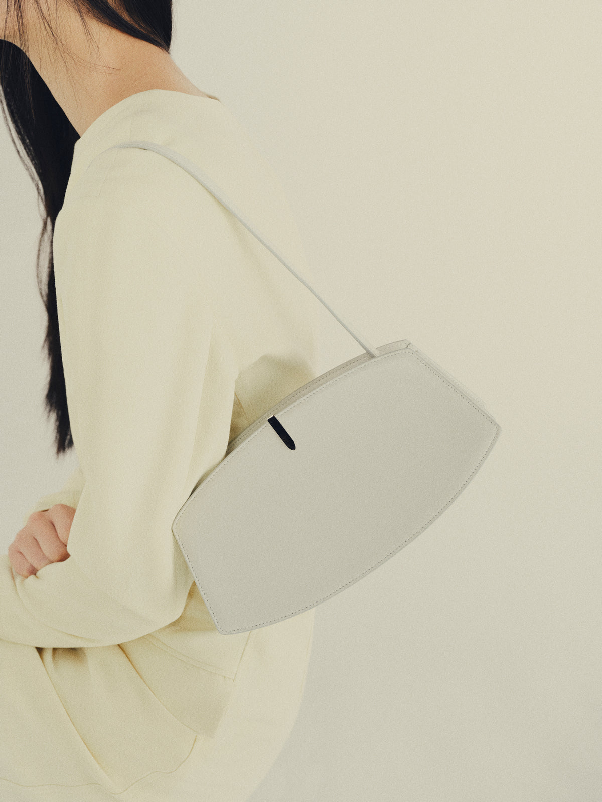 side view of black mesh bag with leather trim and gold clasp on an off white background