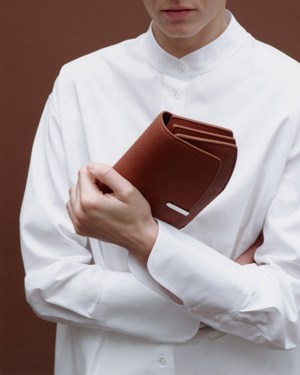 on model image of a brown leather bag with silver hardware on a brown background
