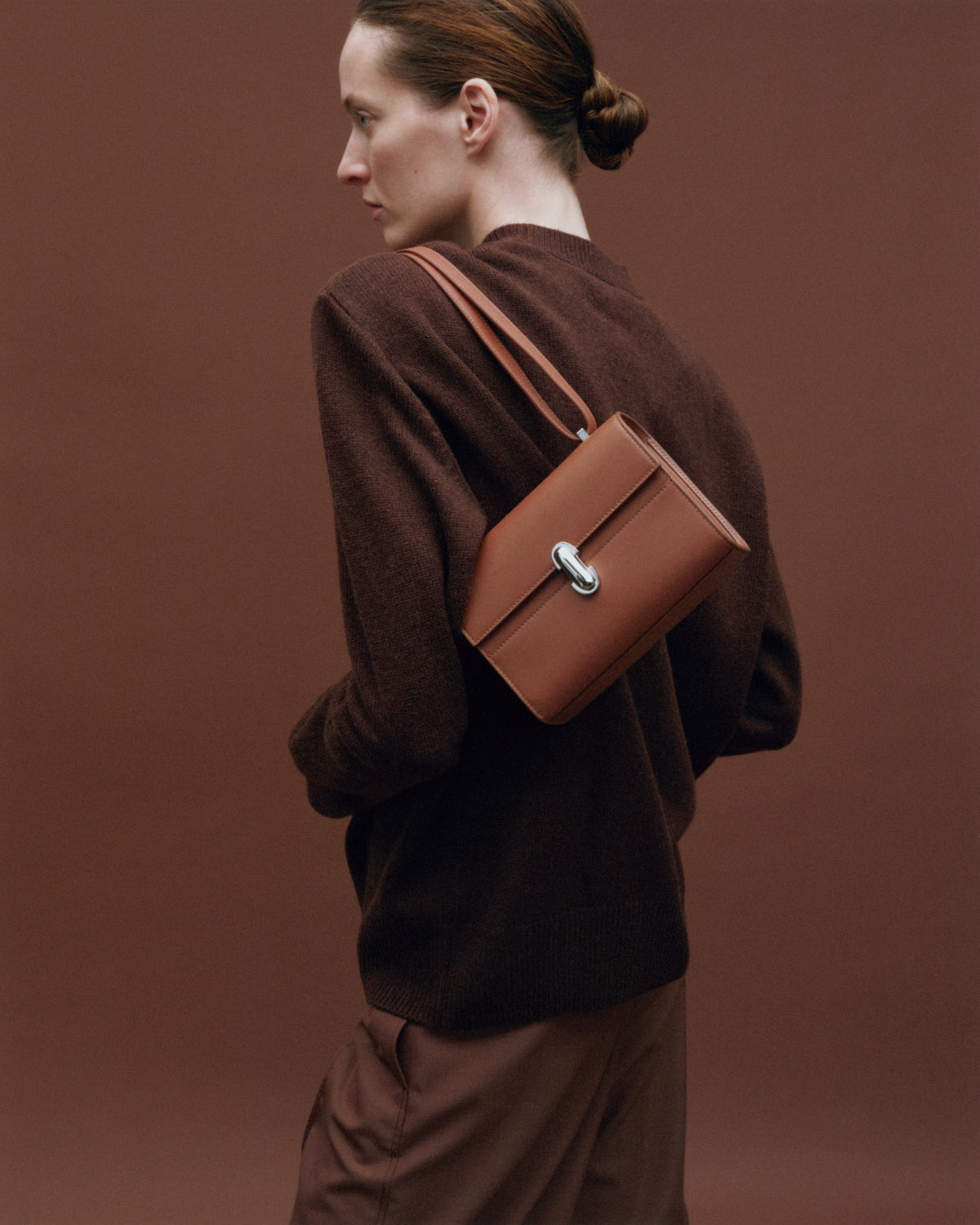 on model image of a brown leather bag with a silver clasp on a brown background