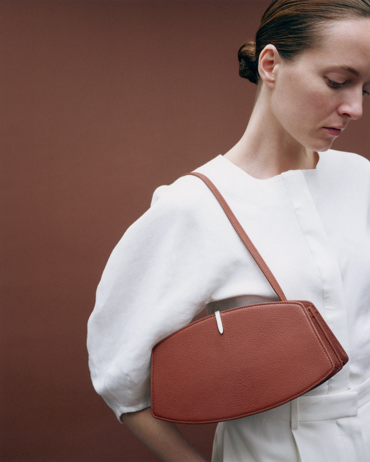 on model image of a maple brown shoulder bag with silver hardware on a brown background