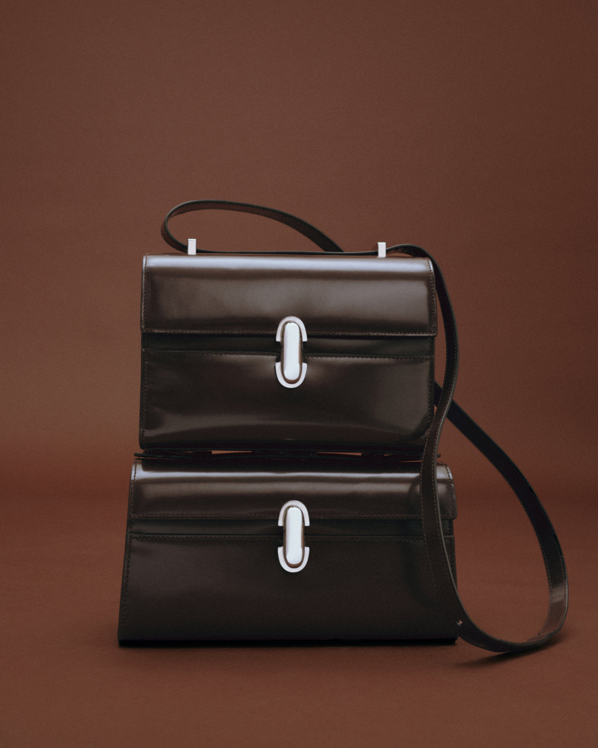 editorial image of two stacked brown handbags with silver clasps on a brown background
