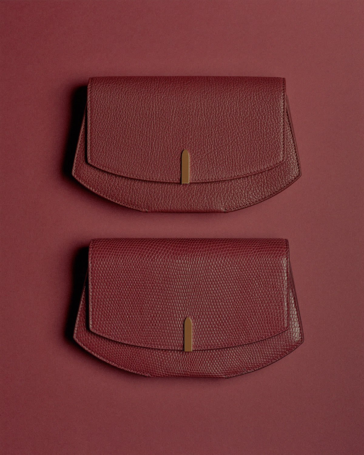 editorial image of two wine red clutches with gold hardware on a red background