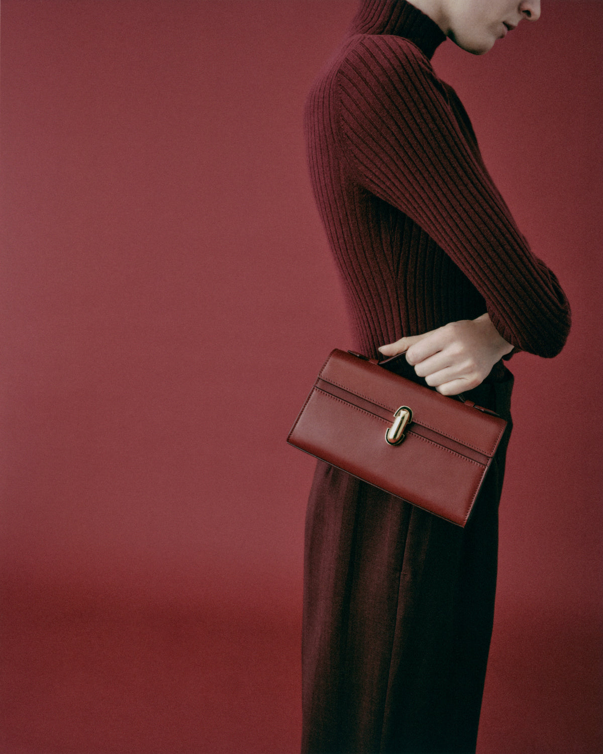 on model image of a wine red bag with gold clasp on a red background