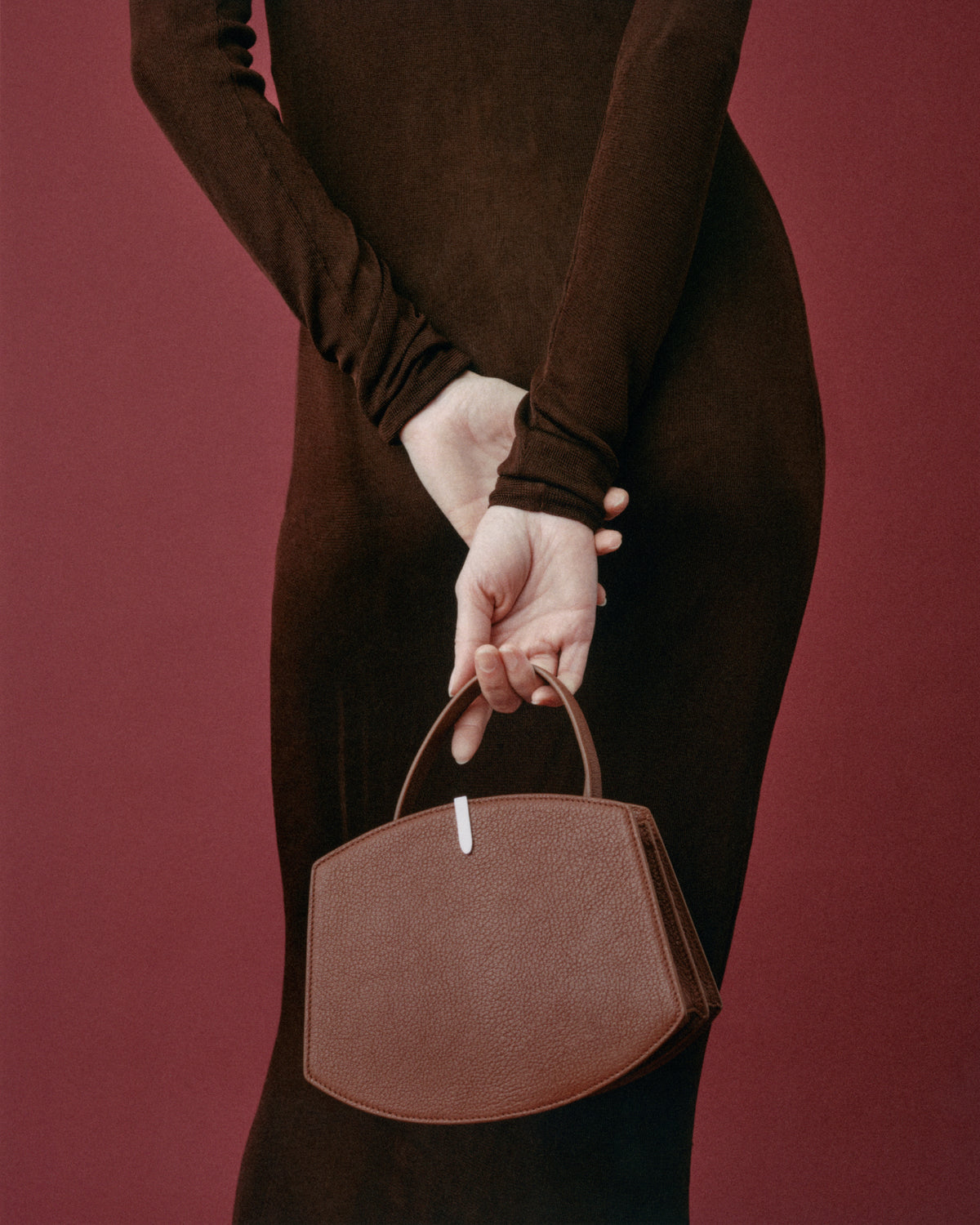 on model image of a brown leather bag with silver hardware on a red background
