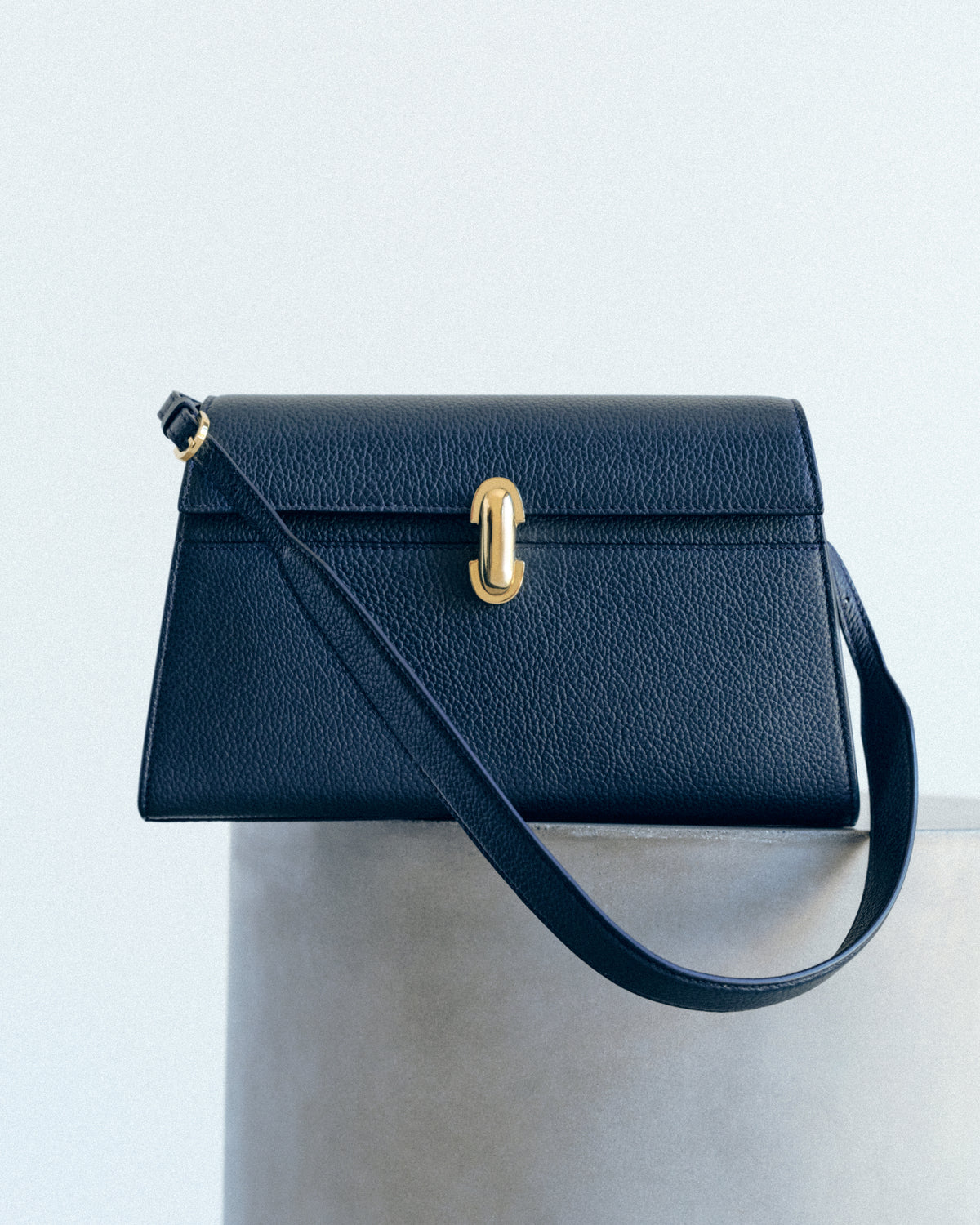 campaign image of navy blue leather bag with gold clasp on a grey background