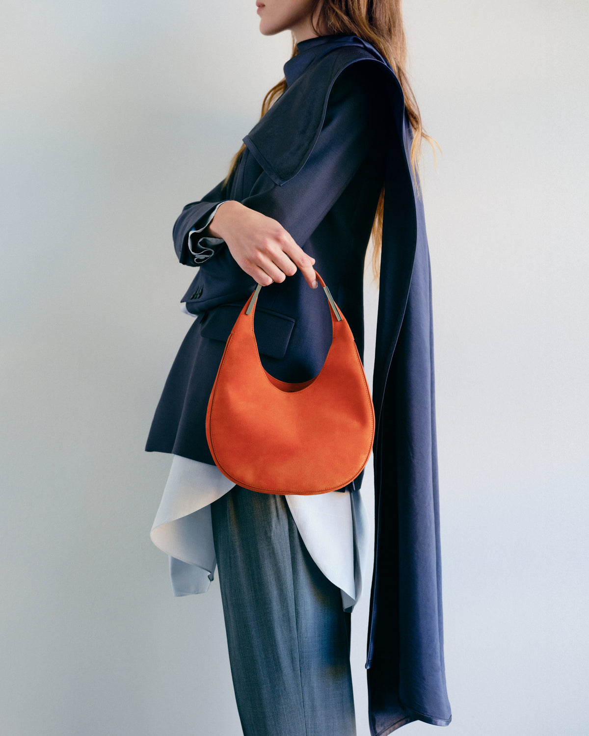 on model image of tangerine orange suede bag with silver hardware on a grey background