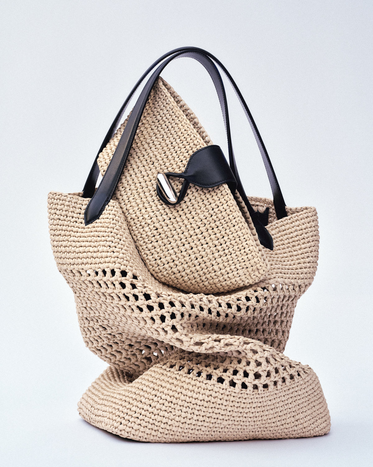 campaign image of two natural raffia bags with black leather trim and silver hardware on a white background