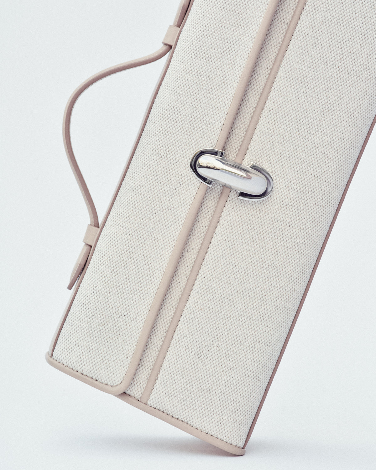 campaign image of a bone beige canvas bag with leather trim and a silver clasp on a white background