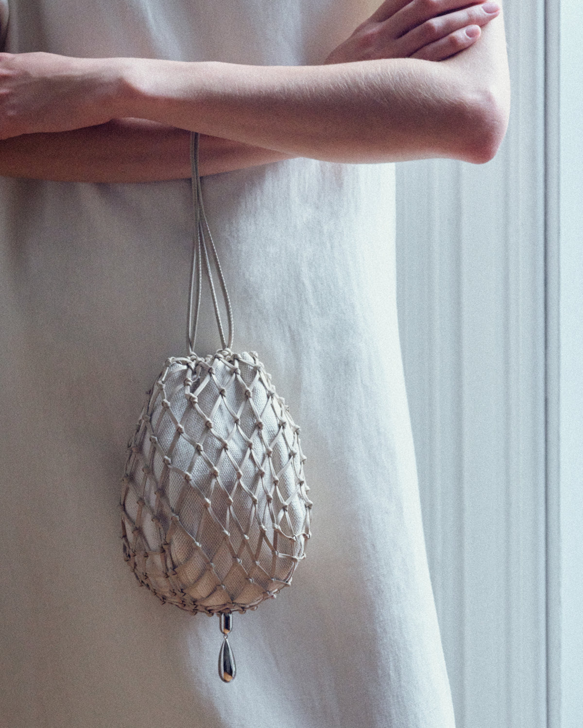 campaign on model image of a bone beige canvas and sheep nappa macrame pouch with silver hardware