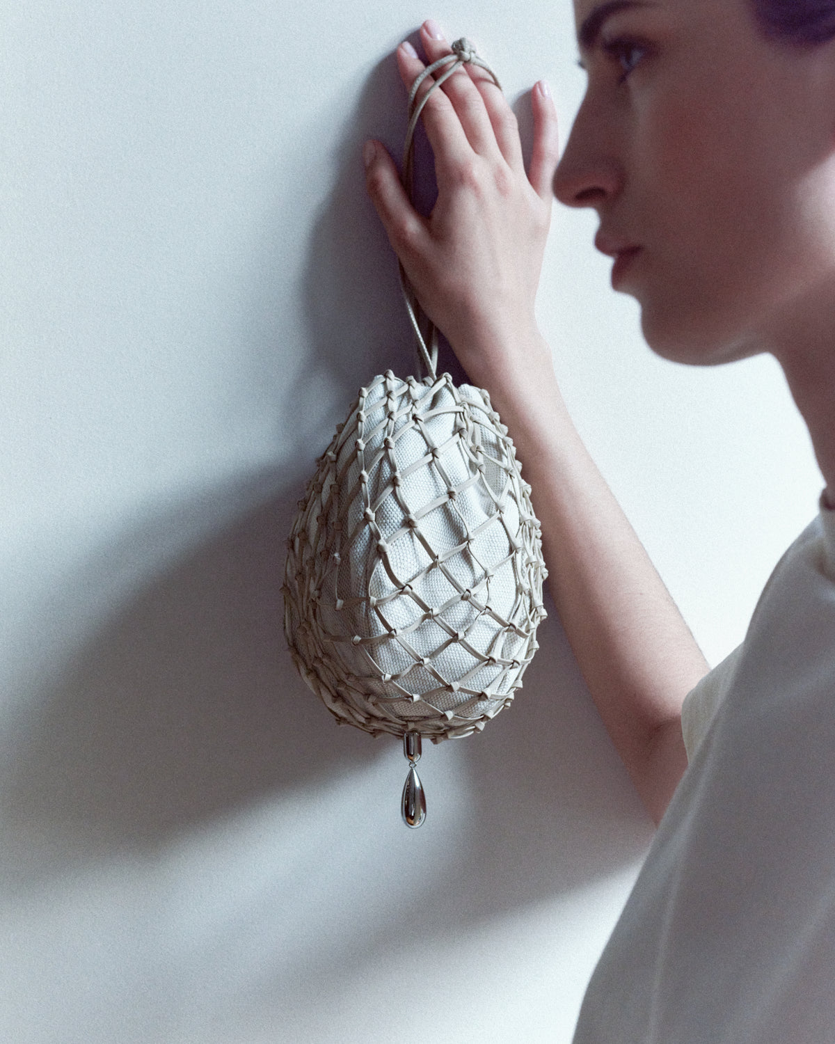 campaign on model image of a bone beige canvas and sheep nappa macrame pouch with silver hardware against a white wall