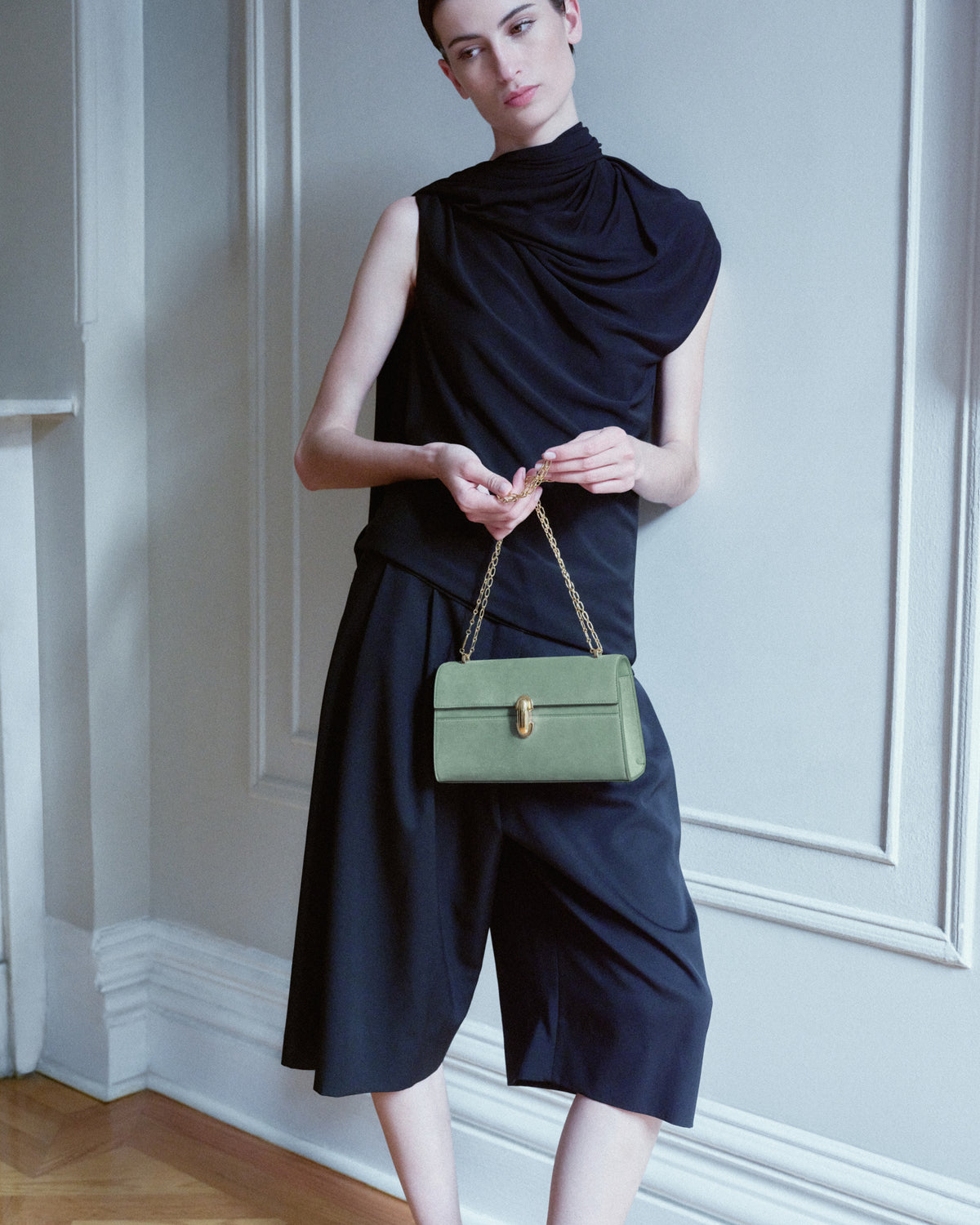 campaign on model image of a cactus green suede bag with a gold clasp and chain