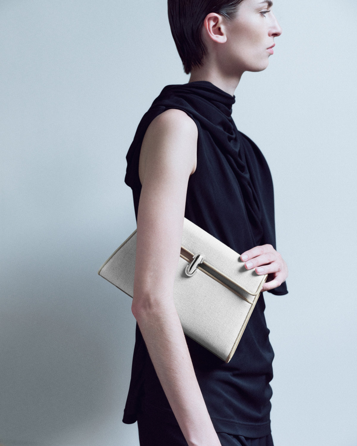 campaign on model image of a bone canvas and leather trimmed bag with a silver clasp on a white background