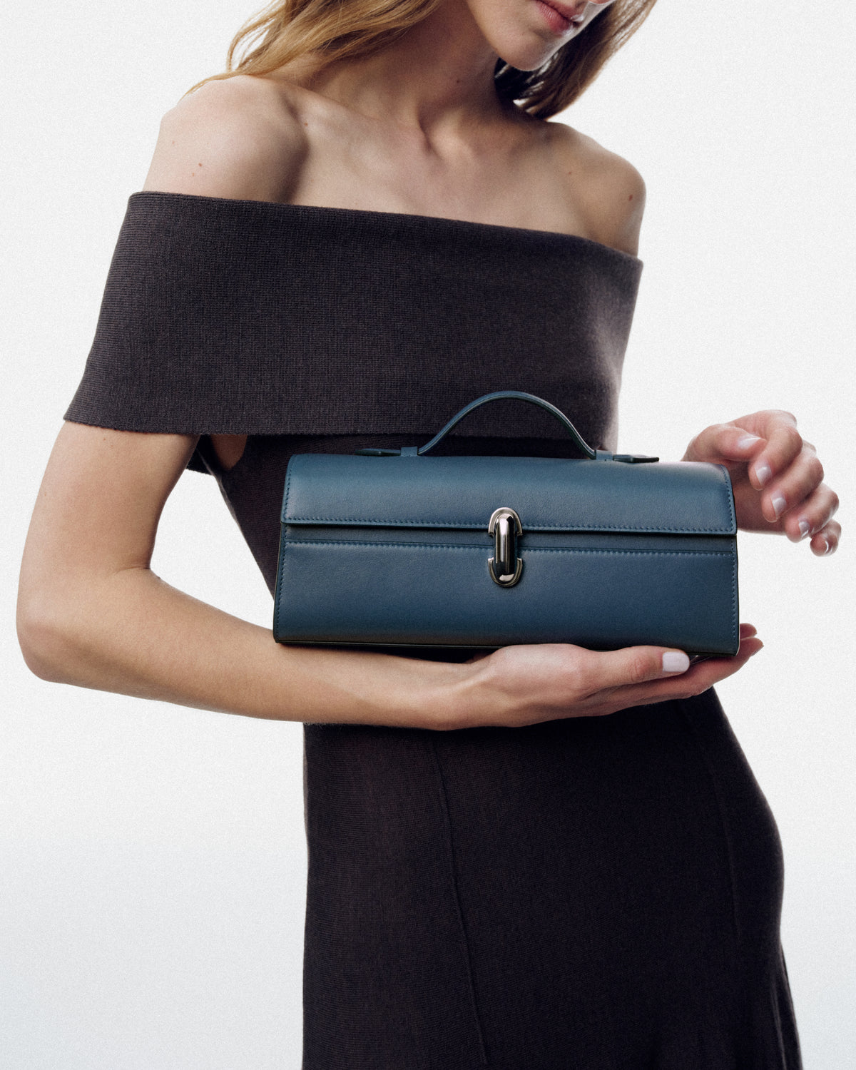 on model image of ocean blue leather bag with silver clasp on a white background