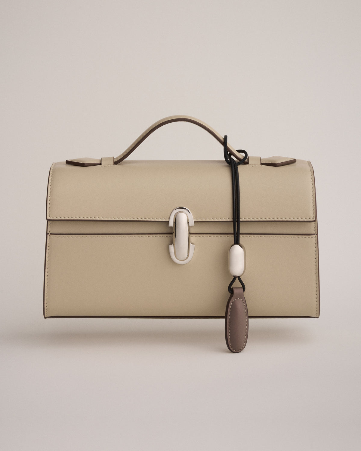 front view of a bone beige leather bag with a silver clasp with a bone beige leather charm on a white background