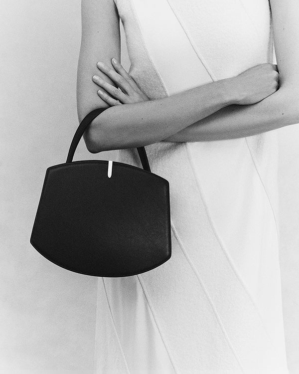 black and white on model image of a black handbag with silver hardware on a grey background