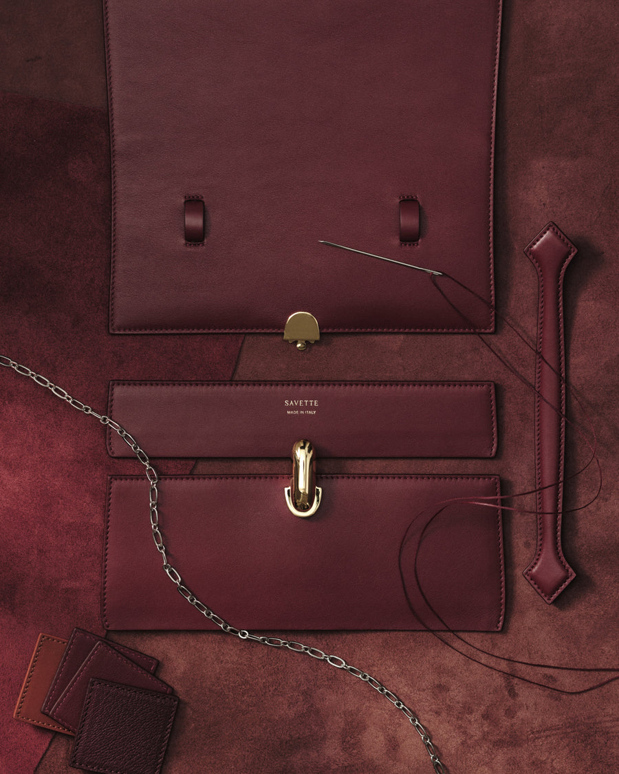 aerial image of deconstructed wine red leather handbag materials with a gold clasp on a red background