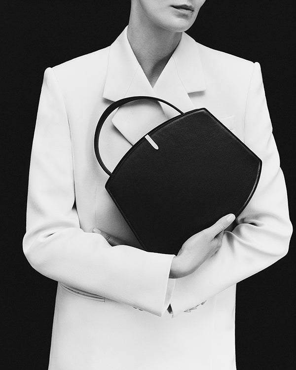 black and white on model image of a black handbag with silver hardware on a black background