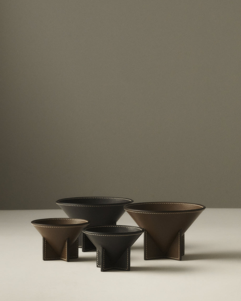 campaign image of two mink brown leather dishes and two ebony black leather dishes on a beige background