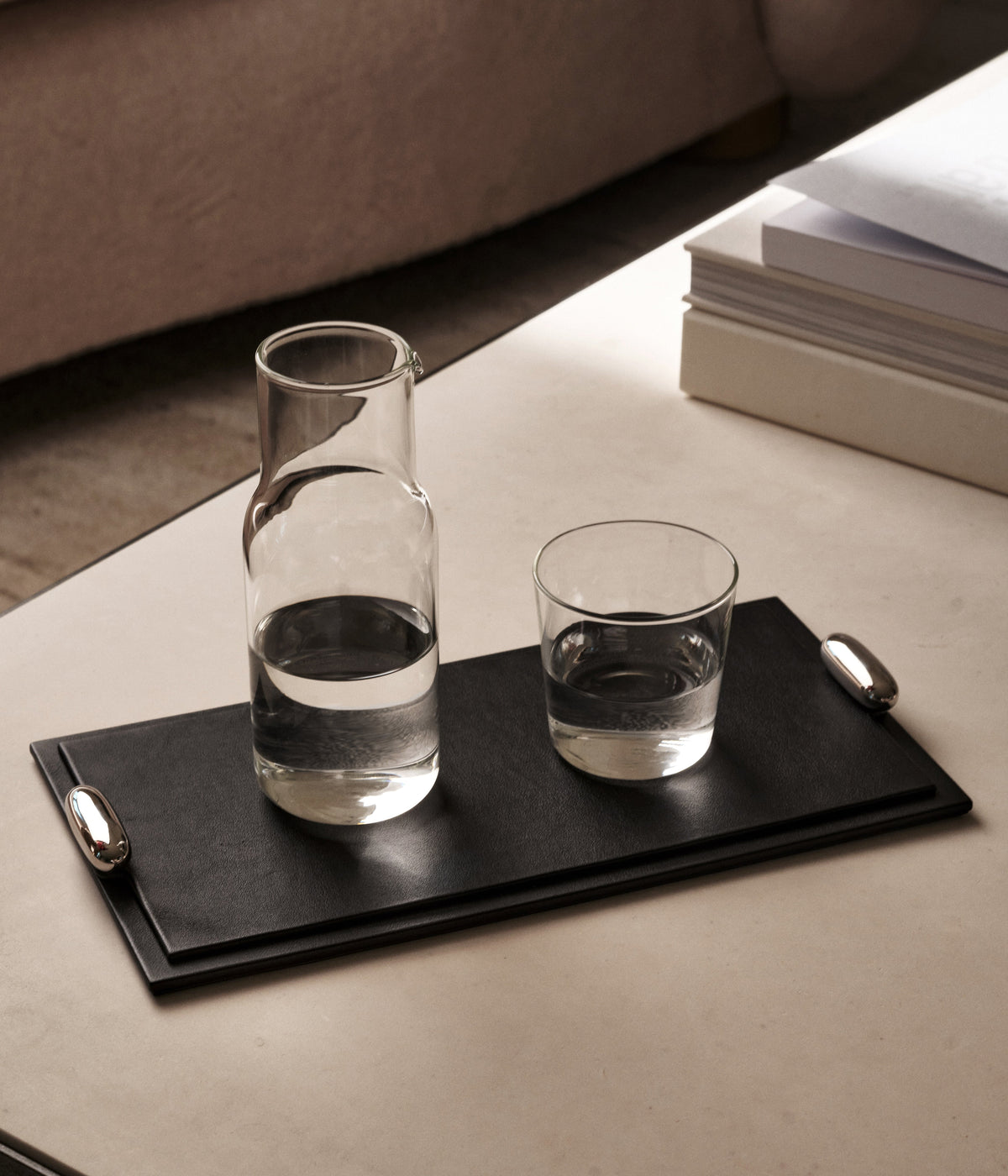 campaign image of ebony black leather tray with silver metal hardware on a coffee table with water carafes