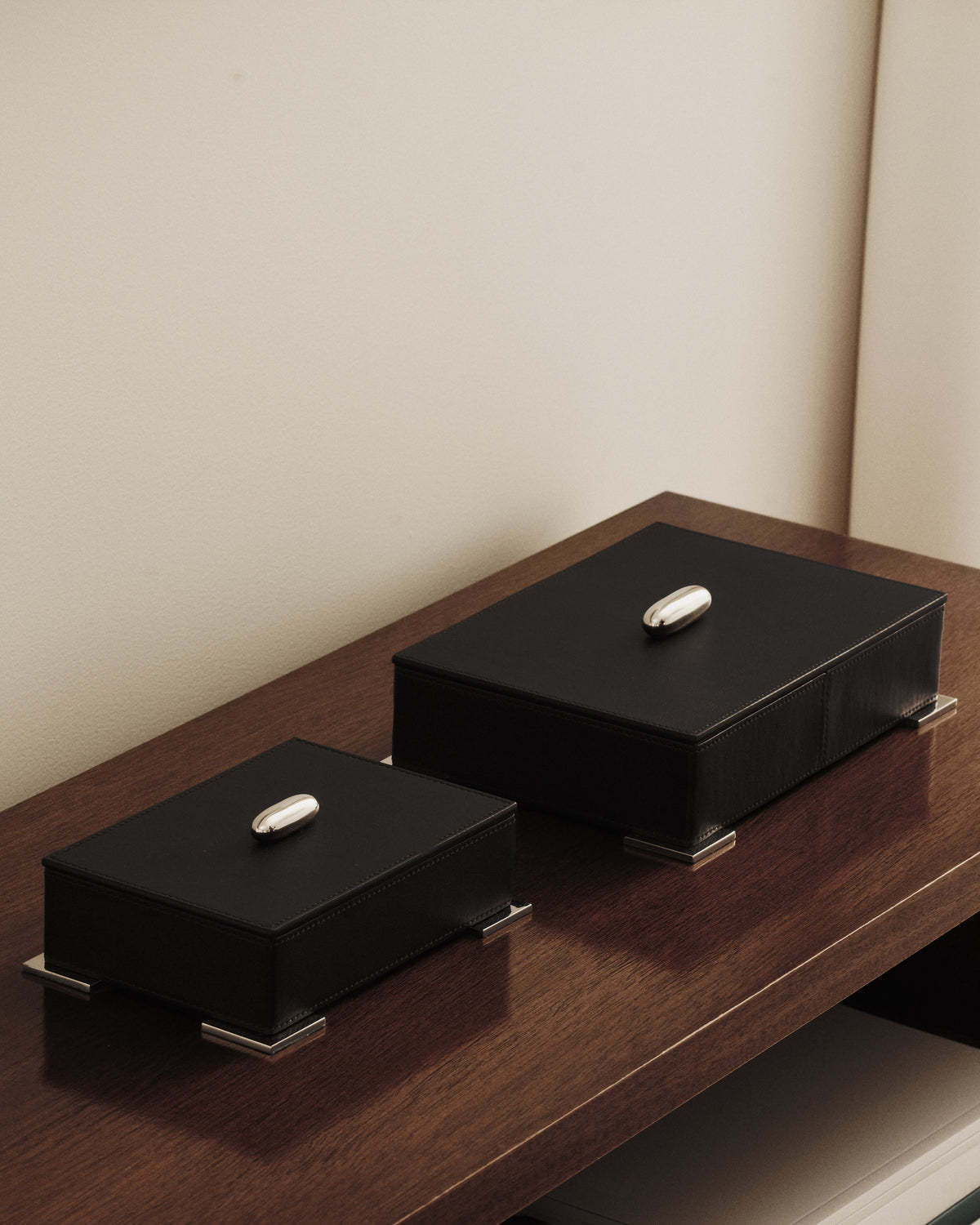 campaign image of two ebony black leather boxes with silver metal hardware on a dark wood table
