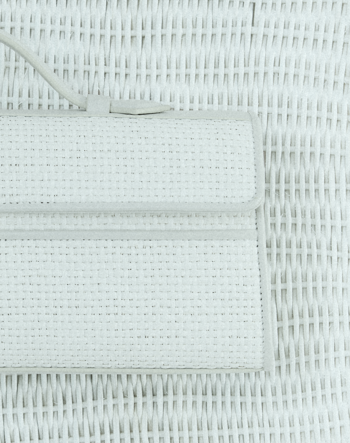 close up detail image of an ivory raffia bag with ivory leather trim on an ivory raffia background